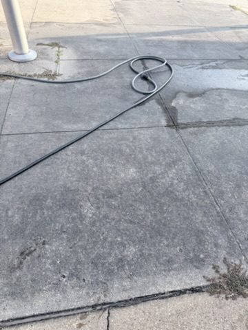 Pressure washer hose on a commercial sidewalk during a surface cleaning job